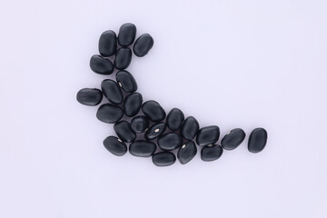 A pile of black beans, arranged in a curve. Top view above shows black beans arranged in a curve isolated on white background.
