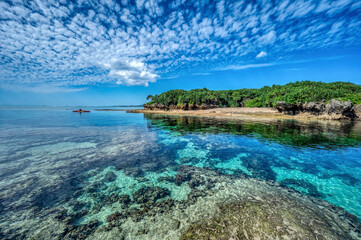 Crystal clear waters of Bise Beach, Motobu District, Okinawa main island. White sand beach with coral outcrops and small islands offshore.