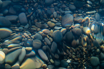 Fototapeta premium Underwater pebble backgrounds. Colorful stones sea bottom in the sun rays. View from above through clear water. Seascape wallpaper texture. Defocus.
