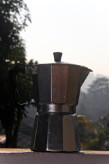 moka pot and a glass of black coffee with a background of nature and trees