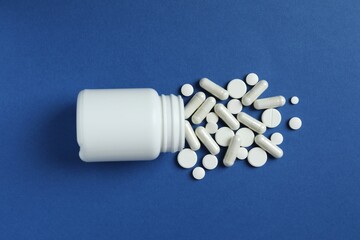 Various pills pouring out of medicine bottle on colorful background
