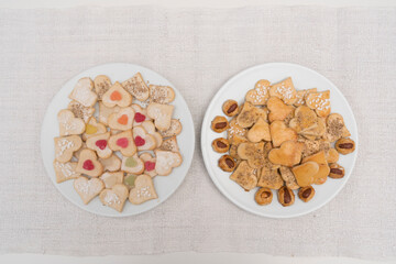 Verschiedene Weihnachtsplätzchen in Herzform auf 2 weißen Tellern auf Leinentischdecke.