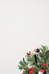 Elegant Christmas vertical banner design with green leaves, red berries, and bullfinches on a white background. Flat lay, top view