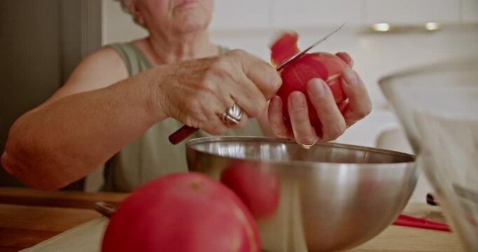 A grandmother carefully peels a tomato over a metal bowl, preparing a meal for her grandson.