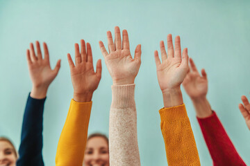 Diverse group of people raising hands in colorful sweaters, expressing enthusiasm and engagement. image captures sense of community and participation