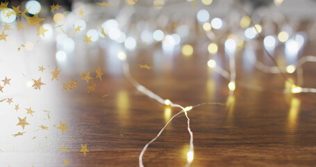 Fototapeta premium Golden stars image over string lights on wooden surface