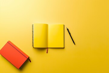 Open yellow notebook with blank pages and a pen on a bright yellow background surrounded by a red notebook