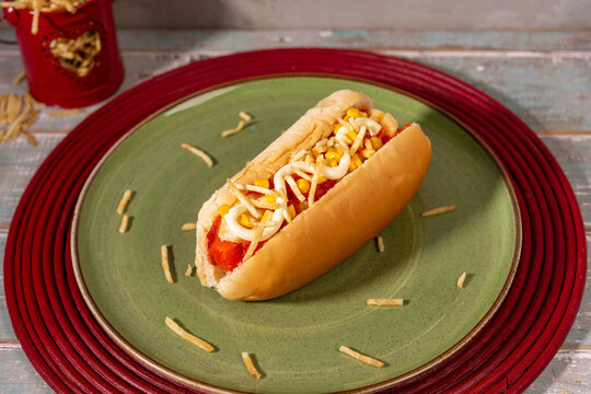 Brazilian Hot dog on green plate with corn and mayonnaise and crispy fries.