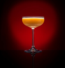 Yellow cocktail in a martini glass on a dark red background.