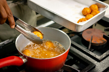 hands frying cheese balls in a pan with boiling oil.