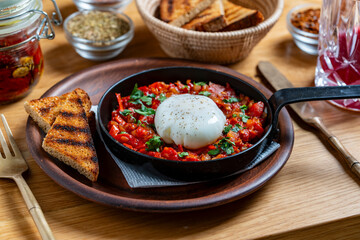 Delicious shakshuka in frying pan for breakfast, closeup. Homemade shakshuka from poached egg, onion, bell pepper, red tomato and green parsley