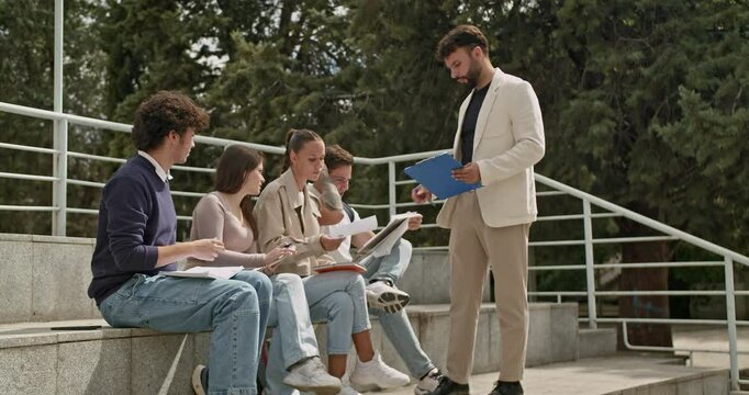 Students solve individual tasks in outdoor class as professor watches and assists. Education, learning, teamwork, teacher, college.
