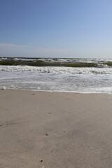 Minimalist View of a Sandy Beach with Ocean Waves. A clean, serene beach scene featuring untouched sand, gentle foam, and rolling waves under a clear blue sky.