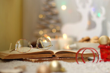 Various Christmas decorations, lit candles, cup of tea or coffee, cookies, books, presents and soft blanket on the table. Holiday hygge at home. Selective focus.