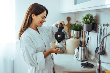 Woman Smiling While Pouring Coffee in Modern Kitchen Setting