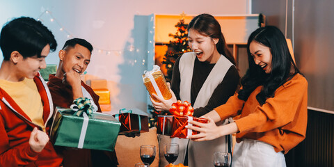 Group of young Asian man and women as friends having fun at a New Year's celebration, holding gift boxes standing by Christmas tree decoration, midnight countdown Party at home with holiday season.