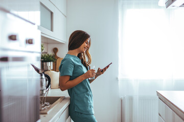 Smiling Nurse In Scrubs Checking Phone While Leaning In Kitchen