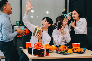 full length view of a group of business team wearing red Santa hat and exchange gift box together in the office for Christmas.