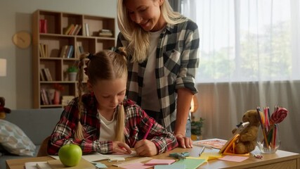 Cheerful Caucasian woman mom mother smile parent female touching little schoolgirl child kid drawing textbook writing at home glad family daughter doing homework girl learning educate custody studying