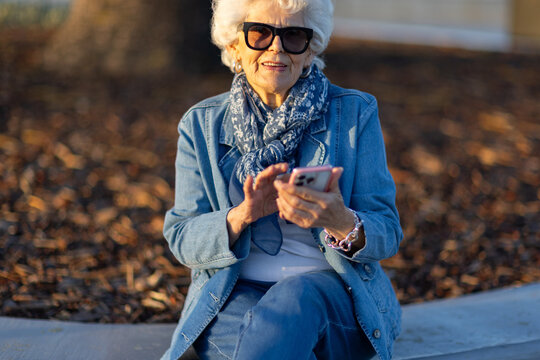 white haired lady in her 80s dressed in denim using a smartphone