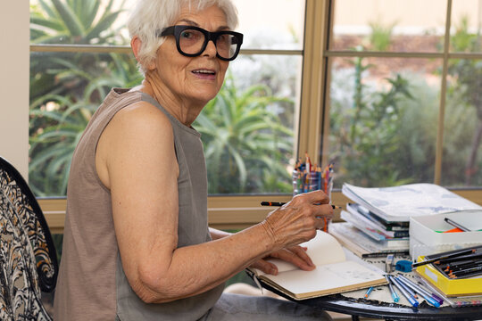 retired lady sitting at her craft table writing or drawing in a notebook