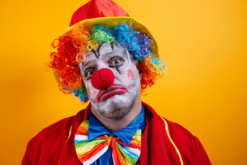 A pensive, sad adult clown on a vibrant yellow background.