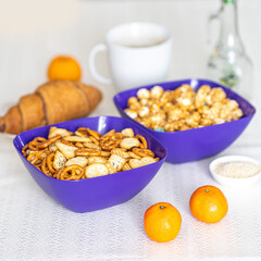 Two blue bowls of snacks and cookies on stone table. Nuts, chips, nachos, crackers.