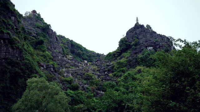 Stunning view of a towering mountain with rocky cliffs, lush greenery, and an intricate staircase leading up to the top. Traditional pagodas and stone pathways enhance the scene peaceful atmosphere