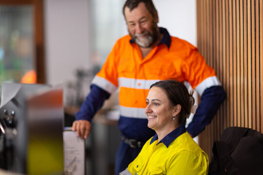 Older man standing beside woman working on her computer in workwear