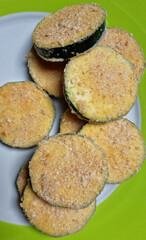 A stack of breaded zucchini slices on a white and green plate