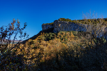 A dramatic rocky cliff surrounded by a vibrant autumn forest under a deep blue sky, capturing the beauty of nature in northern Spain.