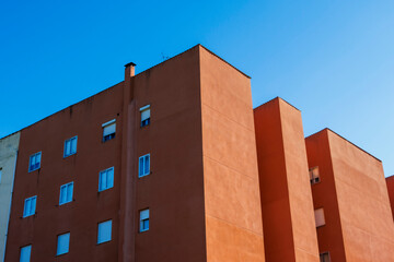 Low-angle view of a modern residential building with a striking orange facade under a clear blue sky, showcasing urban architecture and geometric design elements.