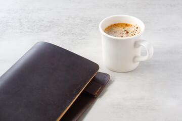 ミルクをたっぷり入れたコーヒー、カフェ・ラッテを飲みながら、茶色の革のシステム手帳でデスクワークをしているイメージ
