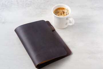 ミルクをたっぷり入れたコーヒー、カフェ・ラッテを飲みながら、茶色の革のシステム手帳でデスクワークをしているイメージ
