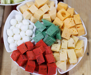 Cheese platter, a variety of cheese cut into cubes. Cheese cubes. White, yellow, green and red cheeses on a plate.