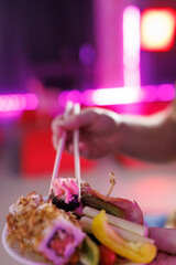 A hand takes sushi from a plate with chopsticks.