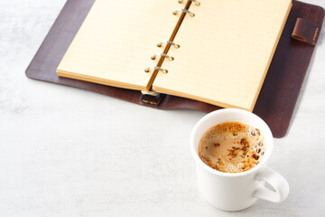 ミルクをたっぷり入れたコーヒー、カフェ・ラッテを飲みながら、システム手帳でデスクワーク中のイメージ
