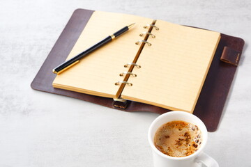 ミルクをたっぷり入れたコーヒー、カフェ・ラッテを飲みながら、システム手帳でデスクワーク中のイメージ
