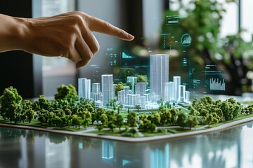 Human hand pointing at a holographic green city model surrounded by trees, symbolizing eco-friendly architecture and smart city technologies. Futuristic urban planning concept.