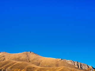 Autumn hills background on blue sky and cloud on sunny day with copy space, walking view at Juta, Georgia. Golden, brown and yellow colors of grass on small mountain range, landscape wallpaper.