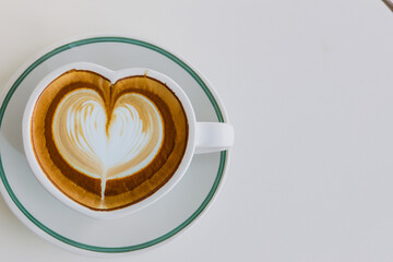 A heart shaped latte in a cup on a white table. A woman is drinking a cappuccino on a gray background. Cappuccino drink gray background drawing heart creative. A creative drawing of a heart lifestyle.