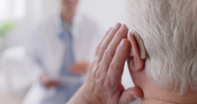 Close-up shot of an elderly man ear wearing a hearing aid during a consultation with a doctor or nurse. The hearing device helps the deaf patient communicate effectively with the medical team.