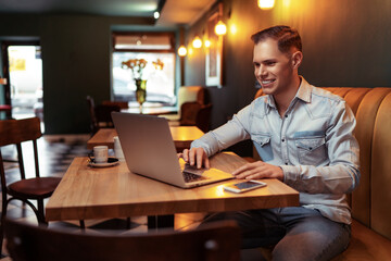 Fototapeta premium Freelance concept. Handsome young man working on laptop computer while sitting at cafe.