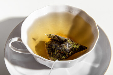Brewing a tea bag in porcelain cup. Black tea in a disposable pyramid tea bag. Strong tea