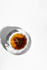 Brewing a tea bag in porcelain cup on white background. Black tea in a disposable pyramid tea bag. Strong tea. Vertical. Copy space