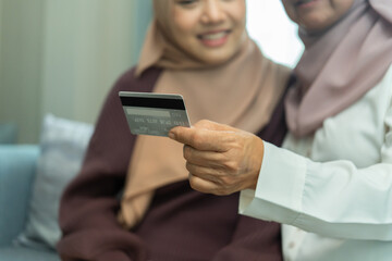 Close-up hand two women wearing hijabs sitting together indoors, smiling warmly as one holds a credit card during their discussion.