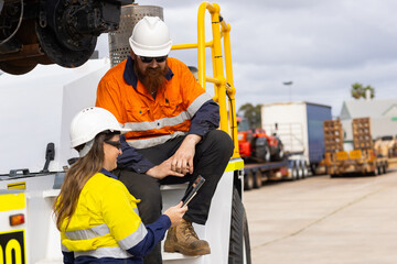 Two workers wearing high visibility clothing man sitting on the truck while woman showing the tablet