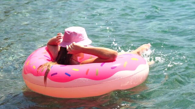 Donut Float, Summer, Water - Young Girl Relaxing in a Pink Donut-Shaped Float on a Sunny Day at the Beach.