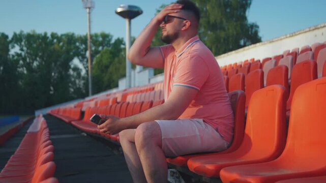 Disappointed stressed emotional fan man on tribune stadium. Lonely man fidgets on stands, supporting team outsiders. Last team of championship, lonely sad upset fan on stadium stands. Fan is worried.