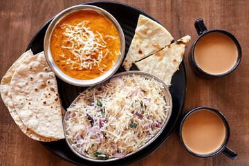 Traditional Indian meal with butter paneer curry, fragrant basmati rice, fresh chapati, naan, and two cups of masala chai tea, served on a rustic wooden table.